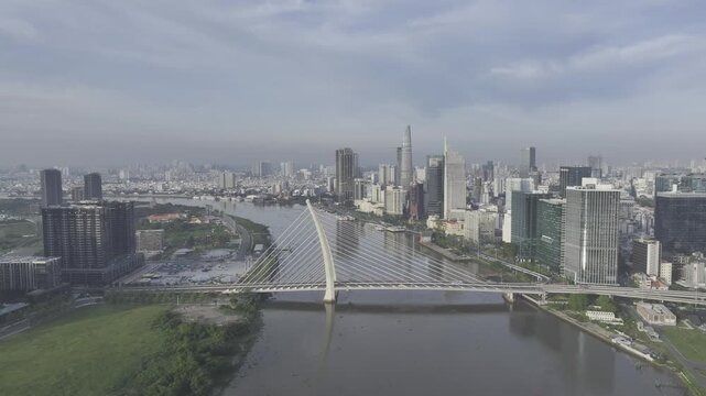 Aerial drone view of Thu Thiem, Saigon River and Ba Son Bridge, with Bitexco Financial Tower in Ho Chi Minh City, Vietnam, illuminated by bright sunlight over the modern urban skyline.