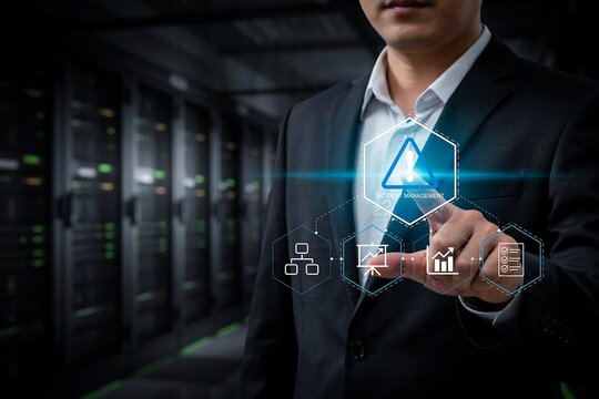 Businessman in a suit touches a warning icon hologram inside a server room data center space