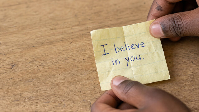 Hand Unfolding Paper Note Saying I Believe in You - Student Encouragement Macro - Youth Empowerment Header - Soft Window Light