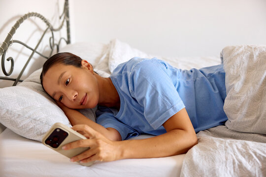 Woman lies in her bed, using the mobile phone