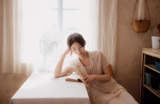 Young woman reading by the window of a rustic wooden cottage
