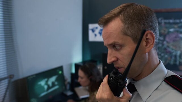 Middle aged Caucasian military officer speaking into walkie-talkie in command center, close up arc shot. Footage is perfect for security training and defense industry marketing