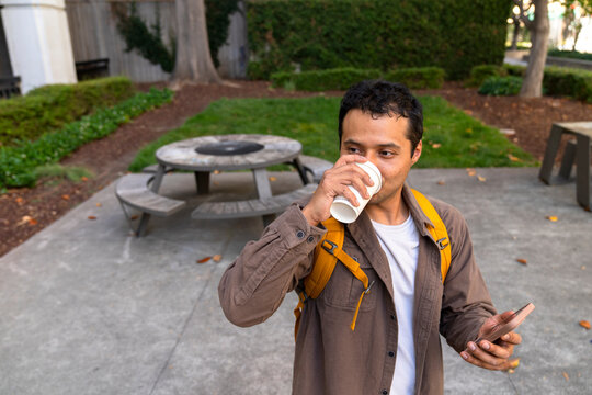 portrait of student drinking coffee cup holding mobile phone on campus