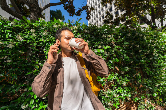 candid city man drinking coffee by greenery talking on mobile phone