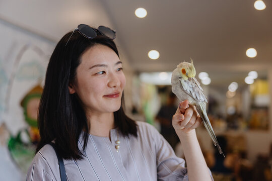 Young Woman Holding Cockatiel Perched on Finger Indoors