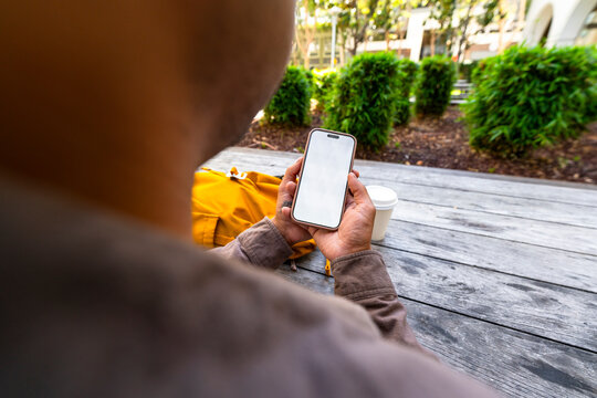 over the shoulder man using blank mobile phone outdoor table city park