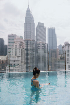 Woman relaxing in rooftop infinity pool with Kuala Lumpur skyline