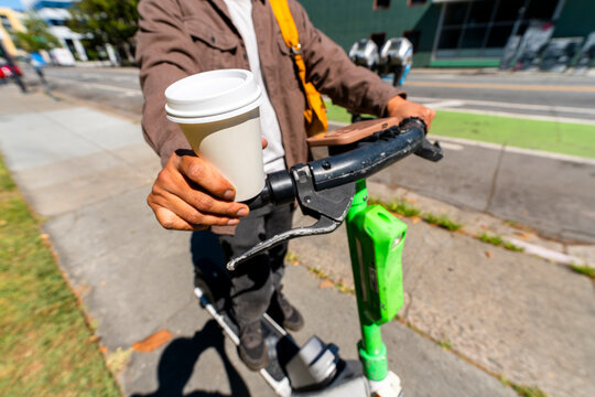 anonymous man holding coffee cup using electric scooter on sidewalk