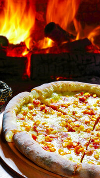 Delicious wood-fired pizza with cheese-stuffed crust, sweet corn, and ham, set against a warm rustic oven fire.