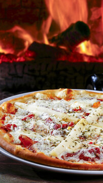Delicious wood-fired pizza with white asparagus, prosciutto, and cheese, baked in a traditional brick oven with a cozy, warm fire in the background.