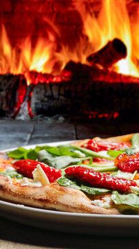 Wood-fired pizza topped with sun-dried tomatoes, fresh arugula, and buffalo mozzarella against a dramatic backdrop of oven flames.