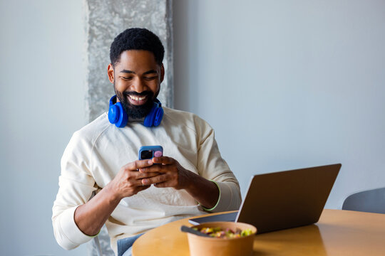 Smiling Man Using Phone While Working on Laptop
