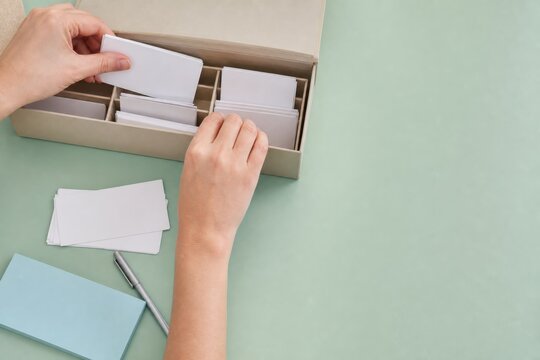 Hands sorting blank business cards into an organizer box on a desk