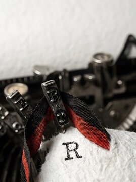 Closeup vintage mechanical typewriter typing letter R with ribbon on textured white paper