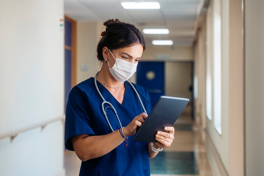 Doctor wearing mask using digital tablet in hospital corridor