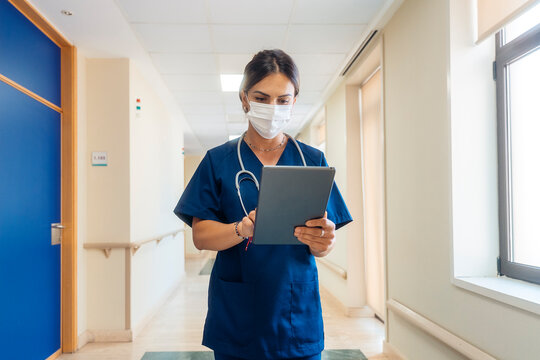 Female doctor with face mask walking and using tablet in hospital corr