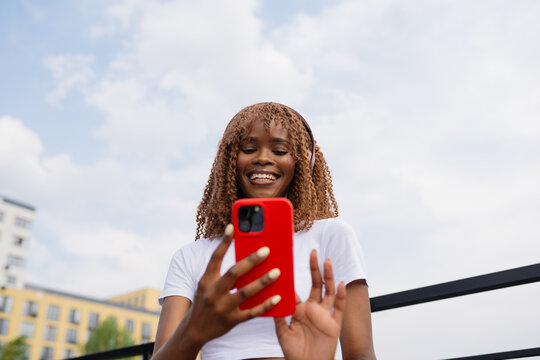 Woman with headphones holding smartphone against blue sky outdoors