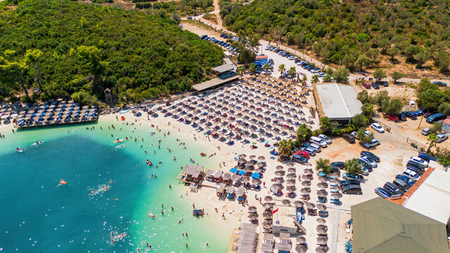 High aerial drone view of the crowded beach, thatched umbrellas, and turquoise water in Ksamil, Albania