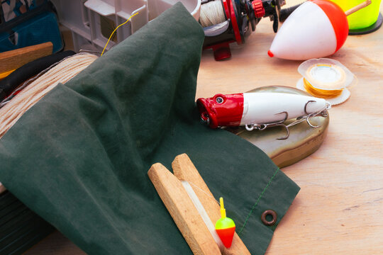 Fishing gear arranged on a wooden surface, showing lures, fishing line, bobbers, and a reel, representing an outdoor hobby and recreational activity