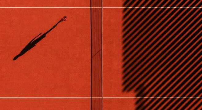 Aerial view of lone figure on red court, long shadow, striped light