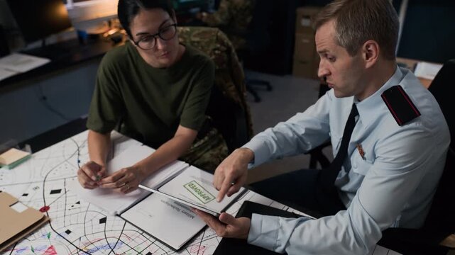 Middle-aged Caucasian male officer and female officer discussing tactical map while using tablet. Tilting up shot ideal for military and defense industry promos