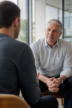 Older man talking with male counselor during a private consultation. Supportive conversation, active listening, mental health care, therapy, and professional guidance in a modern office.