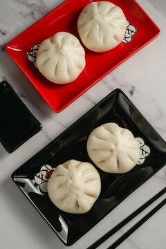 Steamed bao buns served on black and red plates with chopsticks, top view