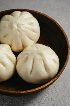 Steamed bao buns served in a rustic wooden bowl