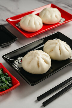 Steamed bao buns with chopped green onion served on black plate