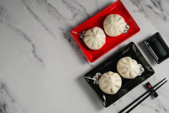 Steamed bao buns served on black and red plates with chopsticks, copy space