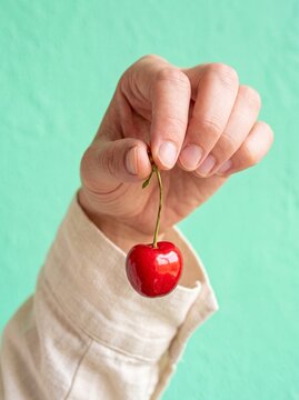 Hand holding a single fresh red cherry against a green background