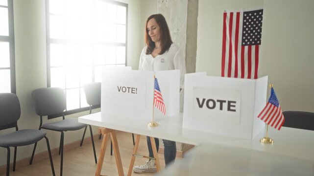 Woman points finger to sticker on chest at voting booth with ballot panels and american flag in polling station building; civic duty pride.