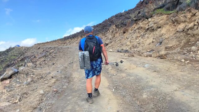 Backpacker walking uphill in rear view on a rough access road on Mount Ararat, Turkey, carrying camping gear for self-supported trekking, expedition preparation, trail access, and mountain travel