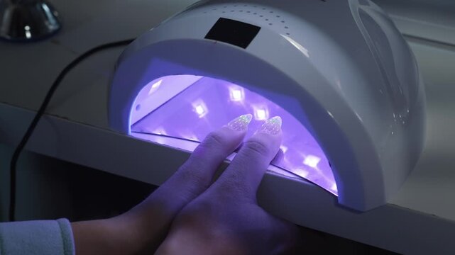 Drying two client fingers in ultraviolet lamp after gel application during professional manicure procedure in beauty salon