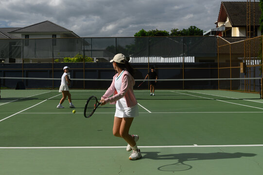 Young Women Playing Doubles Tennis Match on Outdoor Green Court with Opponents Across the Net