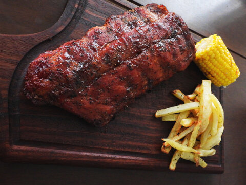 costilla, papas a la francesa y elote a la parrilla presentado en tabla de parota