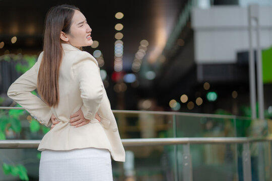 Office syndrome concept showing a businesswoman holding her painful lower back after work, suggesting muscle strain and discomfort. lower back pain, office syndrome, strain, fatigue, posture