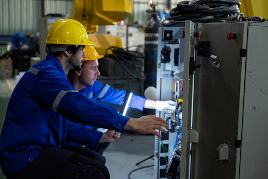 Industrial technician and engineer use an inspection light and tablet to examine a machine control cabinet in a factory. Concept of diagnostics, engineering, automation, safety, and industrial technol