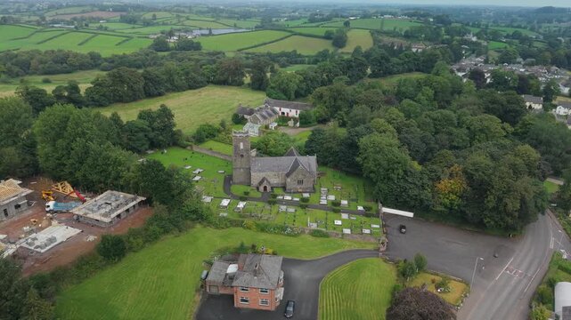 Aerial reveal of St Michael's Church of Ireland and its graveyard beyond the rooftops of Castlecaulfield, County Tyrone, Northern Ireland