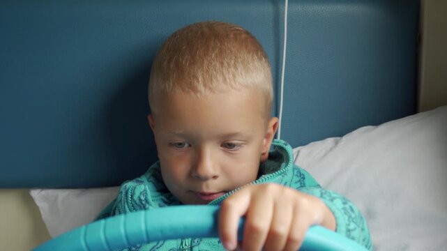 A focused young boy holds a blue tablet while resting on a cozy train bed. His calm, curious expression shows quiet engagement as he relaxes during his peaceful family journey.