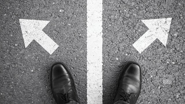 Businessman standing at a crossroads with arrows on asphalt for decision making concept