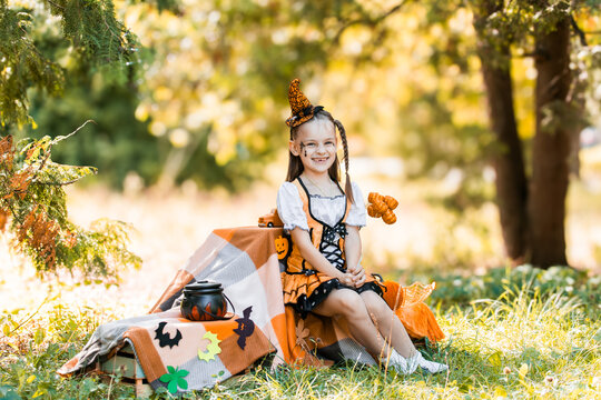 Girl Dressed for Halloween Sits Outside With Pumpkins and Decorations Under Autumn Trees in October
