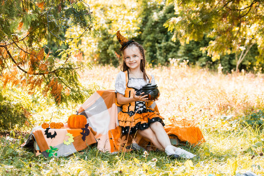 Girl Dressed for Halloween Holds a Pot Among Autumn Leaves and Pumpkins in a Sunny Outdoor Setting