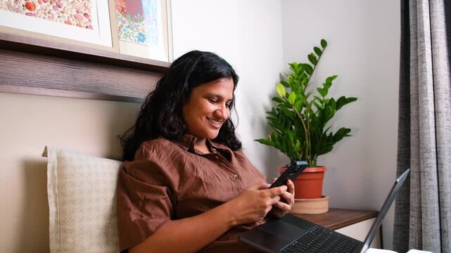 Woman watching reels on smartphone while working on laptop at home, distraction, multitasking, social media addiction, procrastination and remote work concept