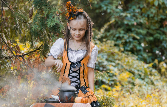 Girl in Halloween Costume Mixes Potion in Cauldron During Autumn Season With Pumpkins and Spiderwebs Around in a Forest Setting