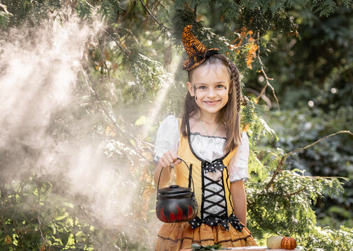 Girl in a Witch Costume With a Cauldron in a Forest During Halloween in October Surrounded by Autumn Leaves and a Spiderweb