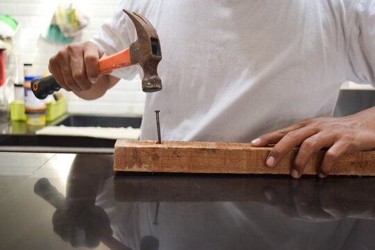 Close up of hands of carpenter holding hammer and knocking in nail the wood