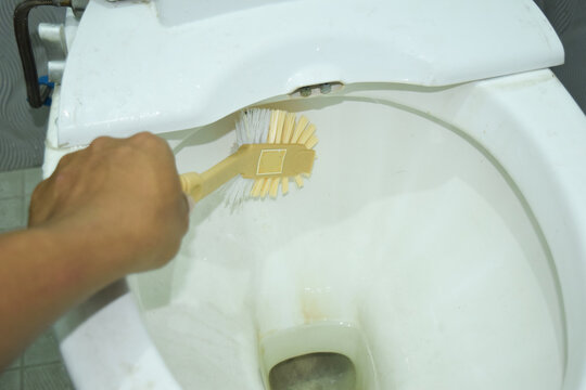 Close up shot of man in cleaning a toilet using a special cleaning product and a brush
