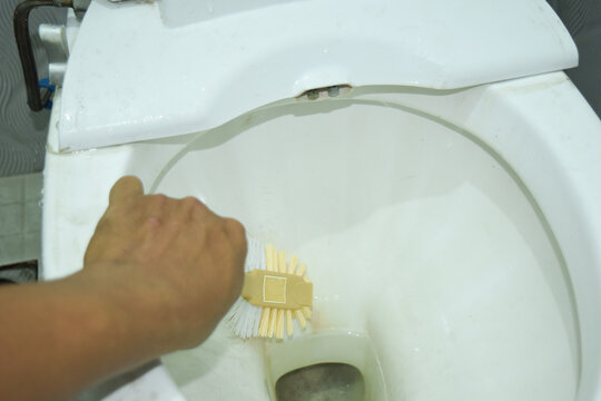 Close up shot of man in cleaning a toilet using a special cleaning product and a brush