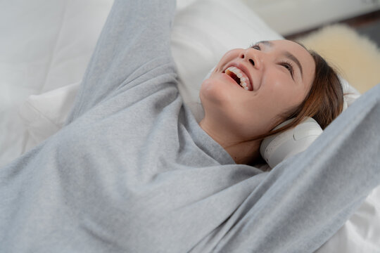 Music relaxation concept with happy young woman wearing headphones while lying on bed at home, smiling and enjoying audio, music, headphones, relaxation, happiness, lifestyle	

